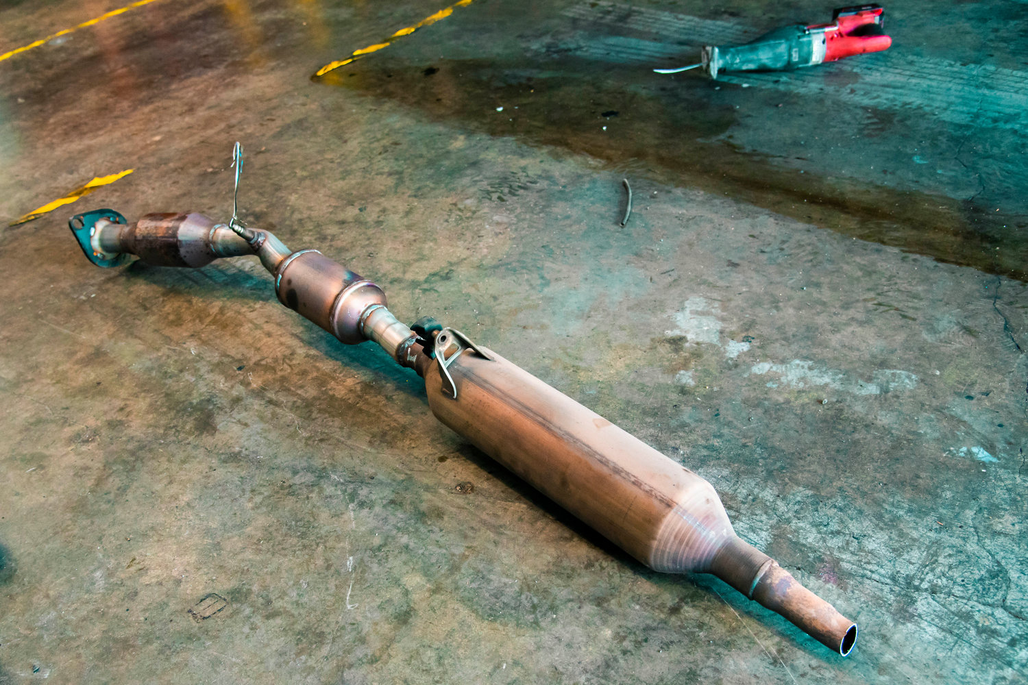 A catalytic converter from a hybrid Prius lays on the floor next to an electric reciprocating hand saw.